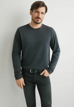 Ciemnoszara koszula z długim rękawem i okrągłym dekoltem, zestawiona z czarnymi dżinsami i czarnym paskiem. Gładka tkanina z minimalnymi detalami szwów.