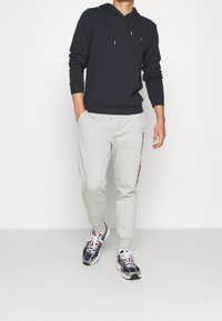 Hoodie navy avec cordons, pantalon de jogging gris avec texte rouge sur le côté, et chaussures de sport multicolores. Design simple et décontracté.