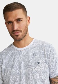 Hvid t-shirt med et mørkt blad mønster, rund halsudskæring og korte ærmer. Inkluderer lille logo detaljeret på forsiden.