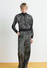 Ensemble de survêtement à imprimé léopard dans des nuances de gris et noir, comprenant une veste zippée avec un col montant et un pantalon à jambes larges assorti.