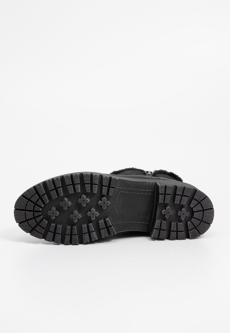Schwarze Schuhsohle mit einem robusten Profil, das erhöhte hexagonale Formen und Rillen für besseren Halt aufweist. Das Material wirkt langlebig und strukturiert.