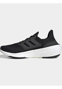 Baskets de sport noires avec semelle blanche coussinée, dessus en maille et trois bandes latérales noires, montrées en profil droit.