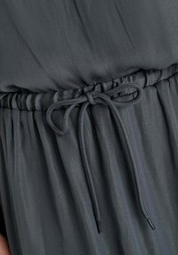 Grijze jurk van lichtgewicht stof met een gerimpelde taille en een trekkoord. Gladde textuur met subtiele plooien en een ontspannen silhouet.