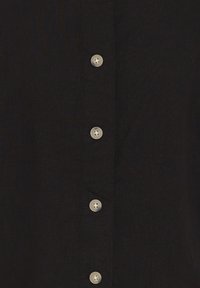 Tissu noir avec une rangée verticale de six petits boutons ronds de couleur claire cousus, disposés uniformément au centre.