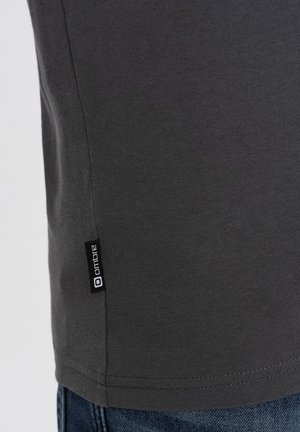 Grijze katoenen t-shirt met een soepele textuur, voorzien van een klein zwart merkteken aan de zoom. Het ontwerp is eenvoudig en aansluitend.