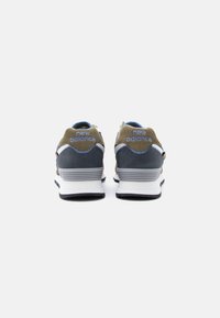 O pereche de adidași New Balance văzuți din spate, cu culori olive, bleumarin, alb și tălpi căptușite gri și albe.