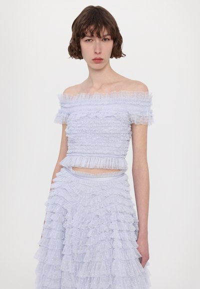 Top azzurro chiaro scollato sulle spalle e gonna coordinata realizzata in tessuto a strati con volant e una trama trasparente a pois. Accentuato da una vita aderente.