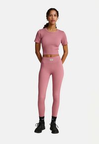 Roze geribd crop-top met korte mouwen, gecombineerd met bijpassende hoge taille legging. Beide stukken hebben een nauwsluitende pasvorm en een minimalistisch ontwerp.