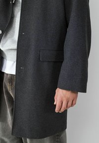 Grau- und Wollmischung Mantel mit geradem Schnitt, versehen mit einer Seitentasche, weiten Ärmeln und einer glatten Textur. Grauer Sweatshirt darunter sichtbar.