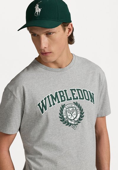Siva bombažna majica s kratkimi rokavi in okroglim izrezom, z zelenim napisom "Wimbledon" in logotipom, katerega sestavljata teniška reketa, nosi pa se z zeleno kapo.