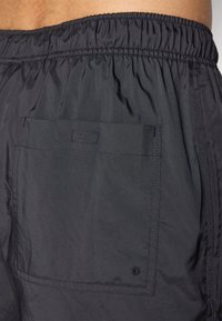 Sorte nylonshorts med elastisk livbånd, med en enkelt baklomme, jevn tekstur og minimale sømdetaljer.