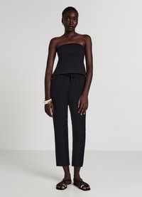 Top nero senza spalline abbinato a pantaloni neri con coulisse e sandali neri con dettagli dorati. Tessuto semplice e liscio con una silhouette aderente.