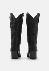 Svart skinn cowboystøvler med spiss tupp, som har intrikate tonale broderier og stablede hæle. To hylster på siden for enkel påkledning.