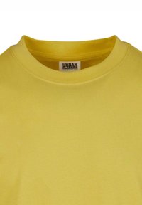Sárga organikus pamut póló kerek nyakkal és rövid ujjakkal, amelynek címkéjén az áll, hogy "URBAN CLASSICS." Sima textúrájú.