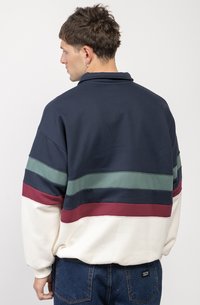 Marineblauwe pullover met brede, meerkleurige horizontale strepen in groen, marineblauw en bordeauxrood. Gemaakt van zachte stof, met een ontspannen pasvorm en lange mouwen.