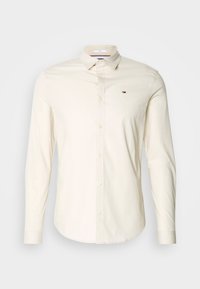 Camicia beige chiaro a maniche lunghe con colletto button-down, realizzata in cotone, con un piccolo logo sul lato sinistro del petto. Tessuto liscio, design aderente.