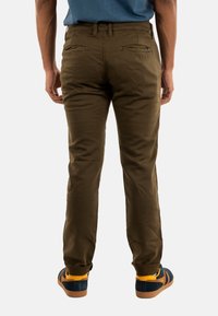 Pantalones de algodón color caqui con un corte ajustado, que presentan bolsillos traseros y puños remangados, combinados con unas zapatillas azules y amarillas.