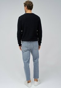 Pull en maille noir, jeans droits bleu clair, baskets blanches. Vue de dos, montrant les poignets côtelés et les détails de la poche arrière.