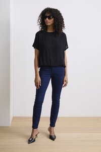 Black short-sleeve top, fitted navy jeans, and black heeled mules. Textured fabric details on the top, smooth finish on jeans and shoes.