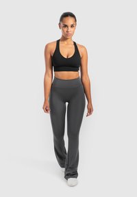 Reggiseno sportivo nero a coste e leggings grigi a vita alta e svasati, caratterizzati da una texture liscia e un design aderente. Le scarpe sono sneakers leggere.