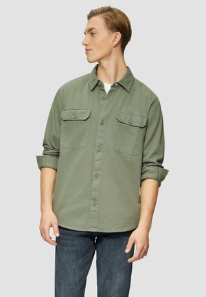 Button-up shirt in olive green, featuring two chest pockets, a fold-down collar, and rolled sleeves. Fabric appears textured and soft.