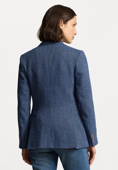 Blazer iz modrega herringbone blaga, pristrižena zasnova z enim zadajšnjim razpočjem, zarezanimi reverji in rjavimi gumbnimi poudarki na rokavih.