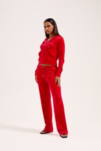 Červený zamatový športový komplet, ktorý obsahuje zipsovú mikinu a nohavice na šnúrku. Slim fit s dlhými rukávmi, bočnými vreckami a nenápadným brandingom.