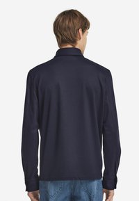 Granatowa polo z długim rękawem o miękkiej teksturze, klasycznym kołnierzyku i lekko dopasowanym kroju. Posiada długie rękawy oraz gładki tył.