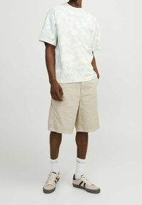 Světle modré tričko s tie-dye vzorem a kulatým výstřihem, doplněné o béžové cargo šortky. Tenisky v neutrálních odstínech a bílé ponožky s černým textem.