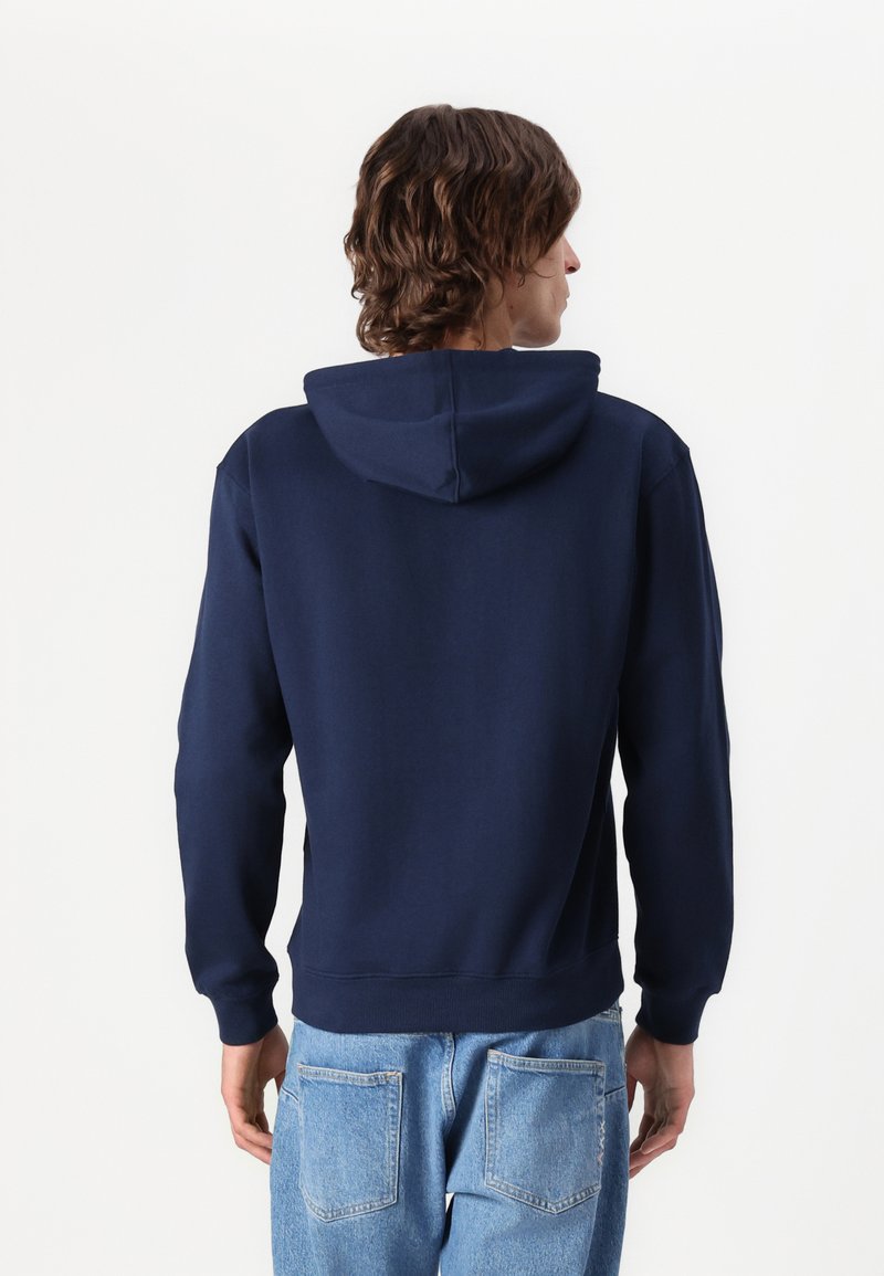 Hoodie en coton bleu marine avec une capuche à cordon et des poignets côtelés. Texture unie, il présente une poche kangourou et une coupe décontractée.