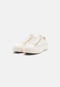 Plátěné tenisky v krémové barvě s pastelovými švy, zlatými průvlakami a texturovanou gumovou podrážkou. Kulatá špička s šněrováním.