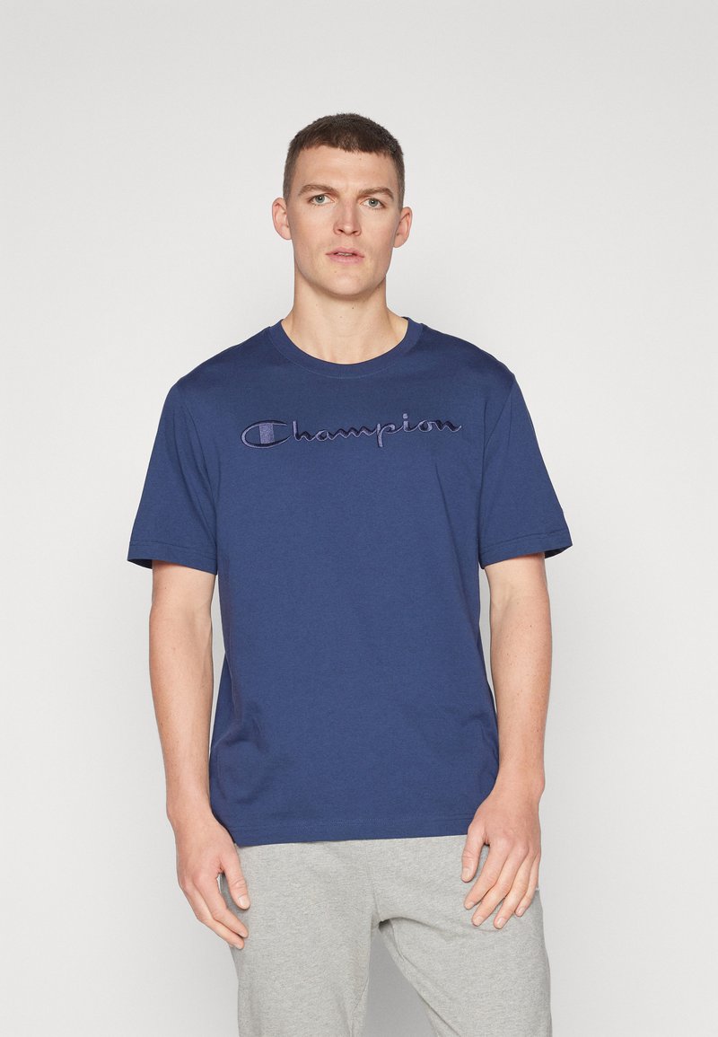 Navyblaue Baumwoll-T-Shirt mit einem großen gestickten "Champion"-Logo in lila Schrift auf der Brust; Rundhalsausschnitt und kurze Ärmel.