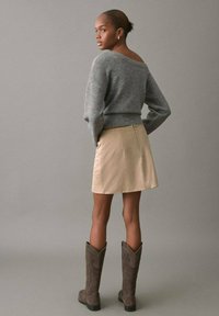 Sivi pleteni džemper, bež mini suknja i smeđe čizme do koljena. Fokus na meke teksture i uski kroj. Jednostavna, neutralna paleta boja.