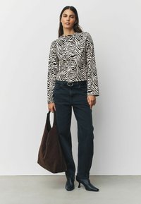 Dlhý rukáv s čierno-bielym pruhovaným vzorom zebry, čierne jeansy so zvýšeným pásom, veľká hnedá semišová taška a čierne špicaté lodičky.