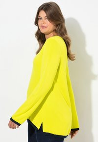 Maglione giallo brillante a maniche lunghe con scollo a V, fessure laterali e polsini blu scuro. Tessuto liscio, vestibilità comoda. Adatto per look casual.