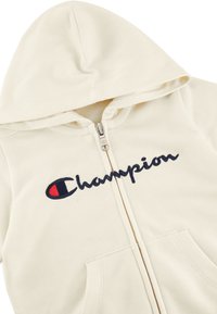 Felpa zip con cappuccio di colore crema realizzata in morbido tessuto, caratterizzata da un grande logo "Champion" ricamato in blu navy con accenti rossi e tasche frontali.