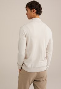 Svetlo bež pulover z rebrastim ovratnikom in manšetami. Mehka tekstura, dolgi rokavi in sproščen kroj. Usklajen s svetlo rjavimi hlačami.