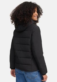 Black puffer jacket with a hood, featuring quilted panels and a lightweight texture, paired with denim jeans.