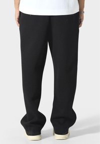 Czarne dresowe spodnie wykonane z miękkiego materiału, o luźnym kroju i zwężanych mankietach na kostkach, w połączeniu z białymi trampkami.