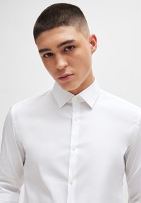 White button-up shirt with a structured collar and long sleeves. Smooth fabric texture with a fitted design. No patterns or accents.