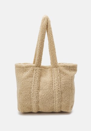 Beige tote-väska gjord av strukturerat, lurvigt material med två robusta handtag och synliga sömmar, med en bred, öppen topp för enkel åtkomst.