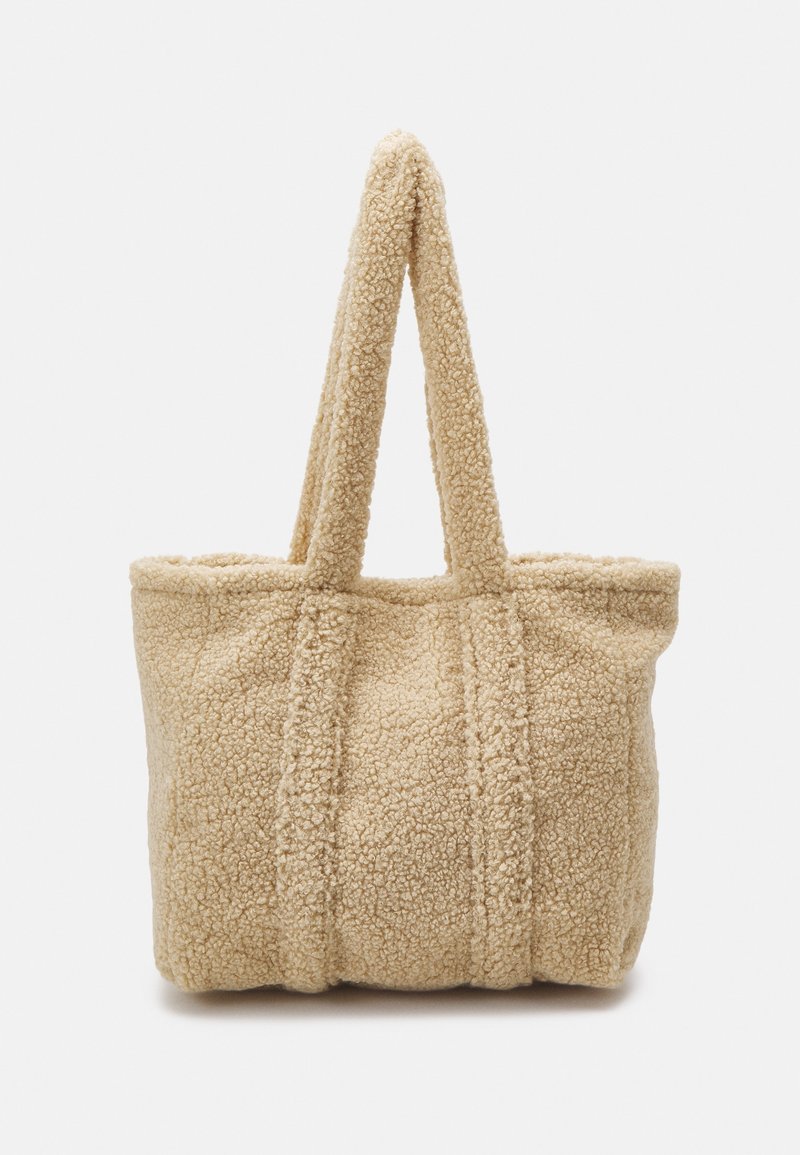 Beige tote bag gemaakt van gestructureerd, fuzzy materiaal met twee stevige handvatten en zichtbare naden, met een brede, open bovenkant voor gemakkelijke toegang.