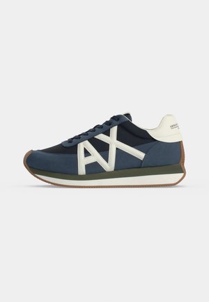 Zapatilla baja en azul marino y azul con franjas blancas con el logo "AX" en los laterales, lengüeta blanca en el talón, suela marrón y cordones negros sobre fondo blanco.