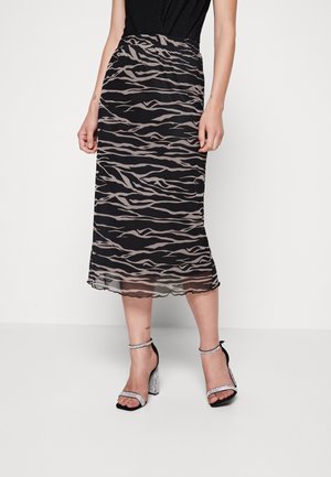 Jupe midi noire avec un motif beige ondulé, texture translucide et ourlet festonné, associée à des sandales à talons argentées.