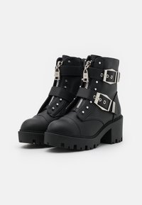 Stivali neri alla caviglia realizzati in materiale sintetico testurizzato, con chiusura a zip, accessori in argento, due cinturini regolabili e un tacco spesso.