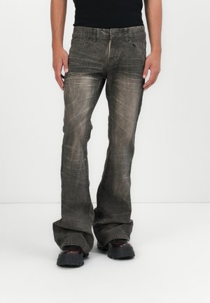 Flared grey jeans with a faded finish and subtle texture details. Features five pockets and a zip fly. Worn with black footwear.