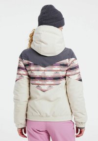 Giacca di corduroy calda in crema con motivi geometrici in rosa, grigio e nero. Presenta un colletto alto, polsini elastici e una vestibilità rilassata.