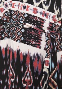Tissu à motifs avec un mélange de dessins rouges, bleus et blancs sur un fond noir ; comprend une ceinture nouée à la taille et des détails texturés.