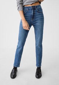 Siniväriset korkeavyötäröiset suorat farkut, valmistettu denimistä. Varustettu napillaisella kiinnityksellä ja hillityllä kulutuksella etuosassa.