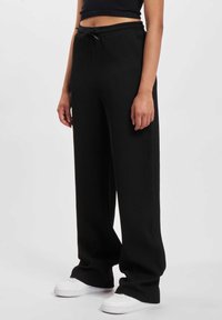 Black ribbed wide-leg pants with an elastic waistband and drawstring closure. Paired with white sneakers. Smooth texture and relaxed fit.